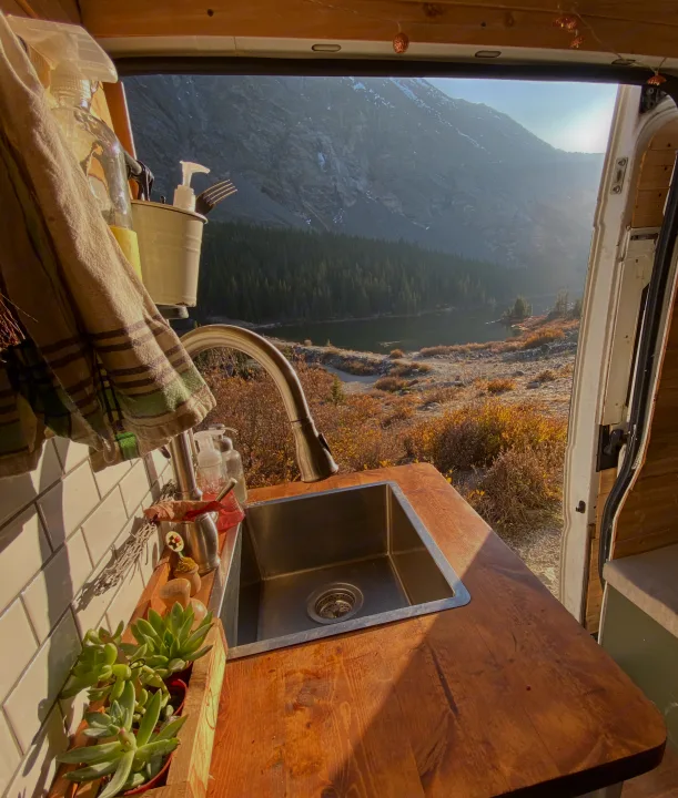 Inside an RV rental: a cozy kitchen with a sink, facing an expansive mountain and lake view through the open back doors.. Other Other 2015