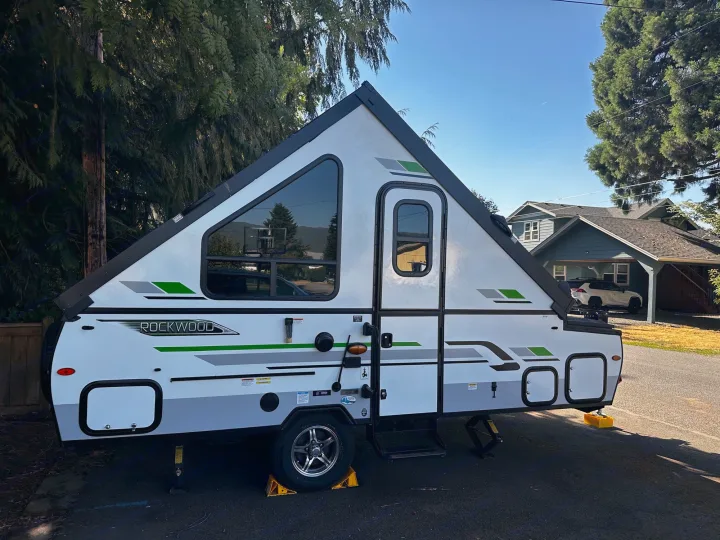This white A-frame Rockwood camper, an ideal RV rental, is parked outdoors. A unique folding travel trailer for your trips.. Forest River A122S 2021