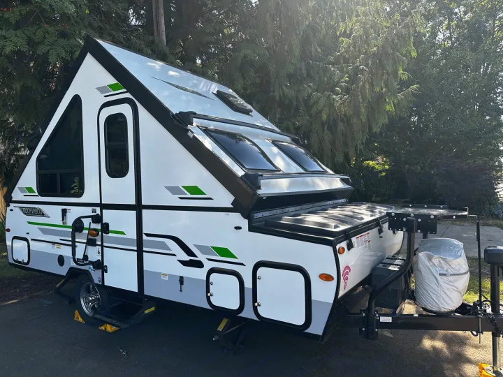 A sleek white Rockwood A-frame pop-up camper with green accents, parked outdoors. Ideal for your next RV rental adventure!. Forest River A122S 2021