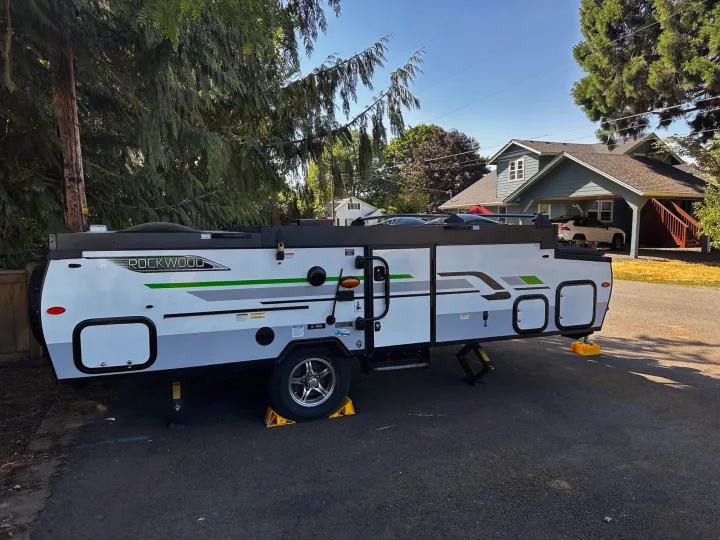 A white and grey Rockwood pop-up camper, perfect for an RV rental adventure, is parked on asphalt. Stabilized for travel.. Forest River A122S 2021
