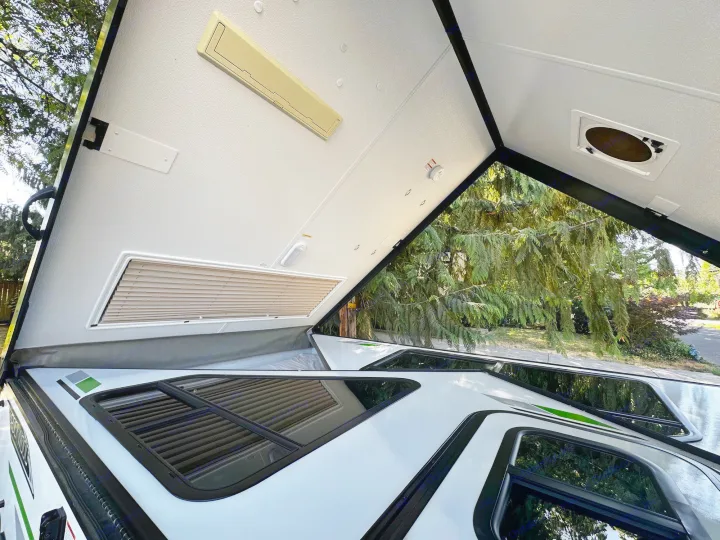 View inside an A-frame pop-up RV: white angled roof, windows, bed, and fixtures. Ideal for your next RV rental trip.. Forest River A122S 2021