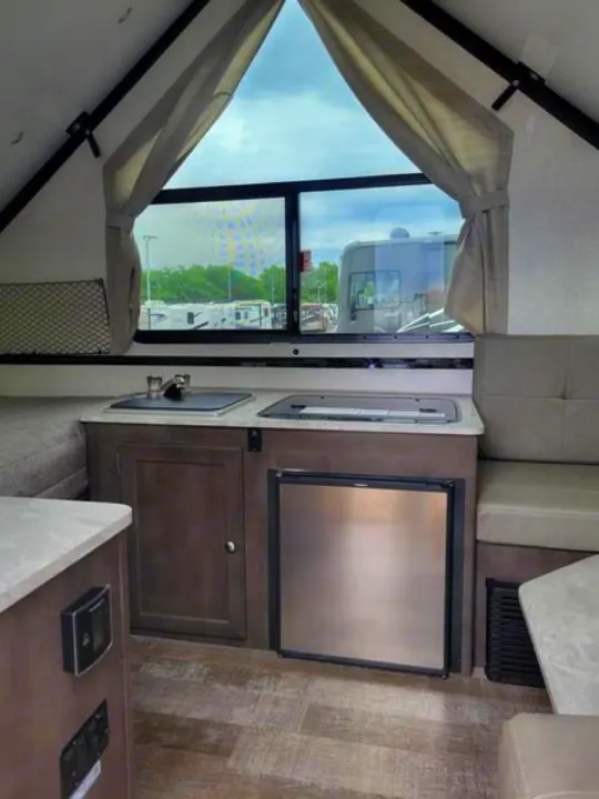 Interior of an RV rental showing a compact kitchen with sink, fridge, and dinette area with large windows.. Forest River A122S 2021