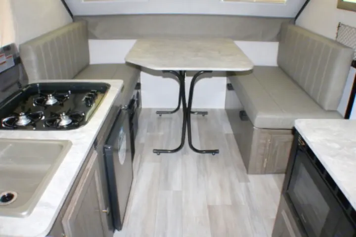 RV rental interior: dinette with table & benches, kitchen area with stove, sink, & microwave. Light wood-look floor.. Forest River A122S 2021