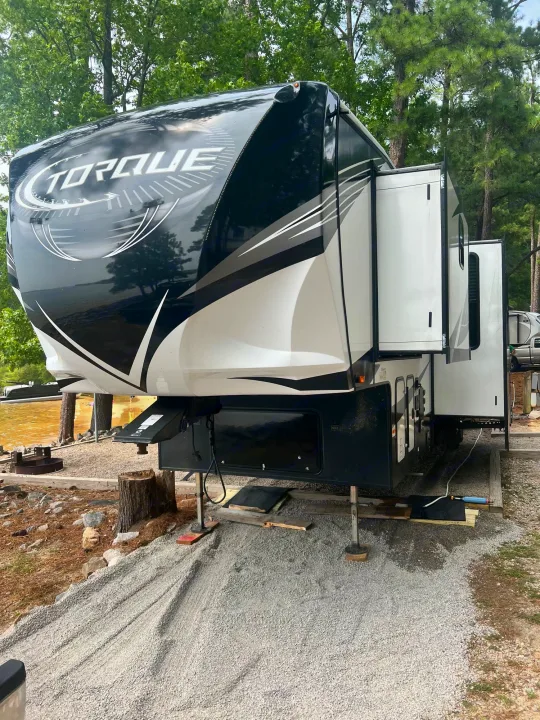 A large Torque fifth-wheel rv rental at a lakeside campsite with slide-outs extended, ready for camping.. Heartland Torque 2020