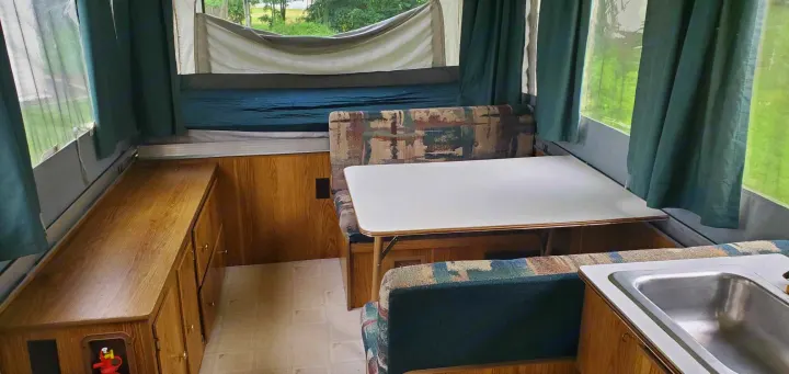 RV rental: Pop-up camper interior showing a dinette with patterned cushions, wood cabinets, and a sink.. Coleman Santa Fe 1997