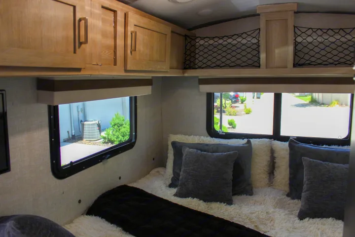 Inside an RV rental: view of a bed with cozy pillows, windows, and practical overhead storage nets.. Forest River Rockwood Geo Pro 2022