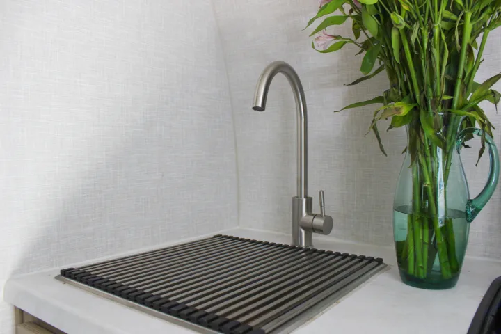 Clean RV rental kitchen area features a brushed metal faucet, a drain rack, and a glass vase with green plant stems.. Forest River Rockwood Geo Pro 2022