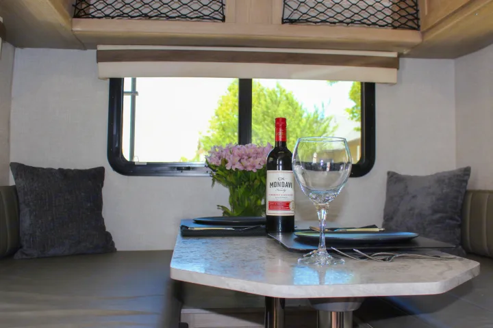 Relax in this RV rental's inviting dinette, featuring wine, fresh flowers, and comfortable seating with pillows.. Forest River Rockwood Geo Pro 2022