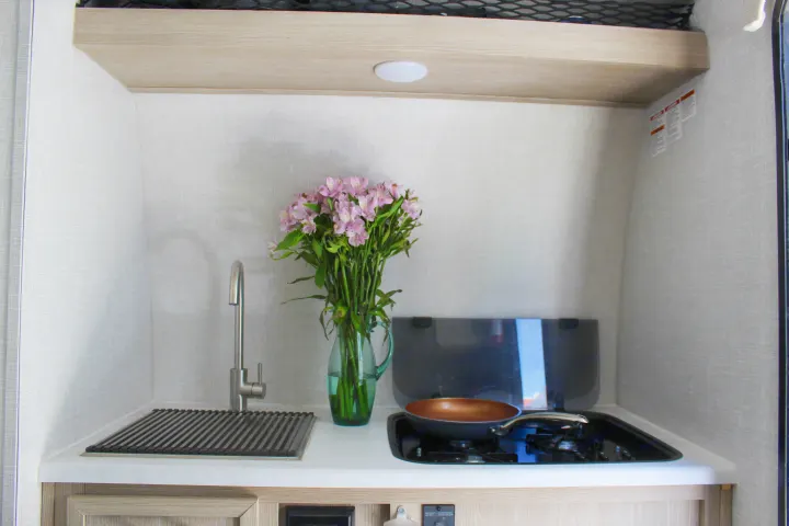 Compact RV rental kitchen featuring a sink, stove, and fresh flowers, ready for your travel adventures.. Forest River Rockwood Geo Pro 2022
