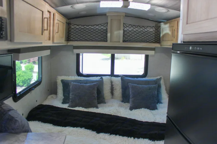 Cozy RV rental bedroom featuring a plush bed with white and gray pillows, overhead storage, and windows with outdoor views.. Forest River Rockwood Geo Pro 2022