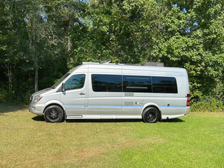 This silver camper van parked on green grass with trees, perfect for an RV rental.. Winnebago Era 2017