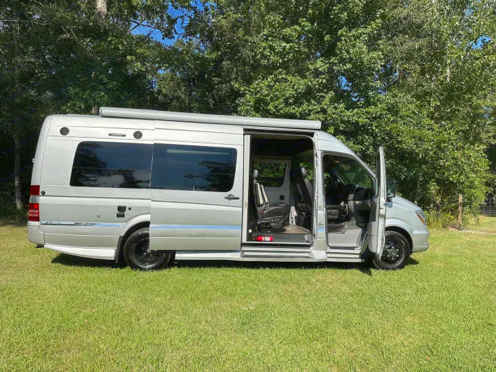 A silver camper van, perfect for rv rental, parked on grass. Its side and front doors are open, revealing the interior.. Winnebago Era 2017