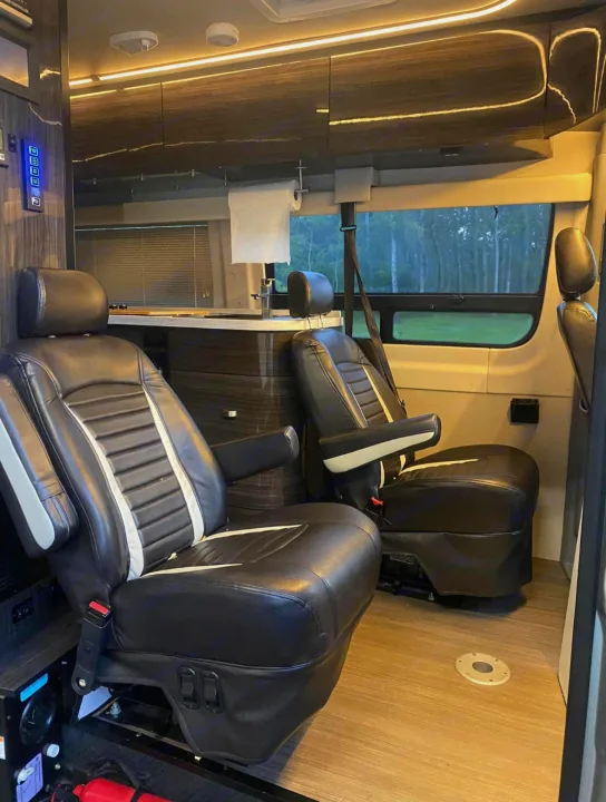 Spacious RV rental interior featuring two black leather captain's chairs, a compact kitchen counter, and forest views.. Winnebago Era 2017