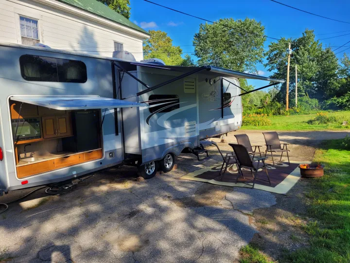 An inviting RV rental scene: a travel trailer with an extended awning, outdoor kitchen, chairs, and a cozy fire pit.. Highland Ridge RV Roamer 2016