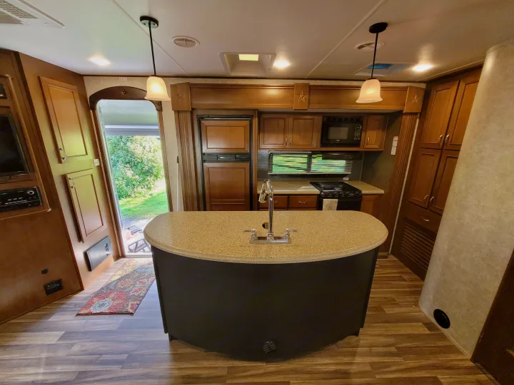 Inside this RV rental: a spacious kitchen with an island sink, stove, microwave, and wood flooring.. Highland Ridge RV Roamer 2016