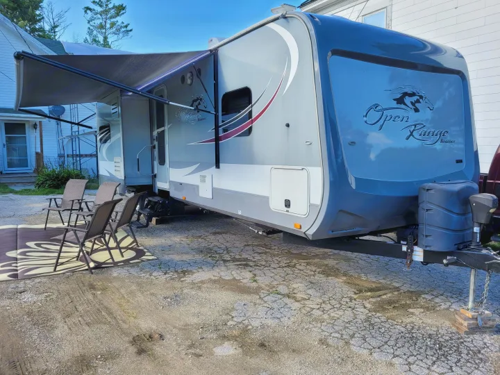 Explore this Open Range travel trailer RV rental, featuring an extended awning, outdoor mat, and chairs setup.. Highland Ridge RV Roamer 2016