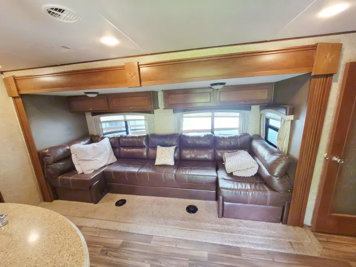 Spacious RV rental living area featuring a large brown leather sectional sofa, ample windows, and wood-accented cabinets.. Highland Ridge RV Roamer 2016