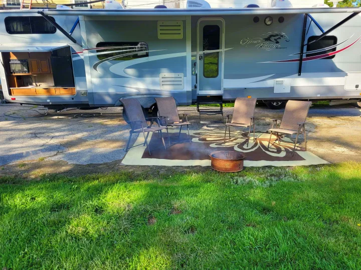 RV rental outdoor setup: A gray camper with an open kitchen slide, awning, chairs, and a fire pit on a patterned rug.. Highland Ridge RV Roamer 2016