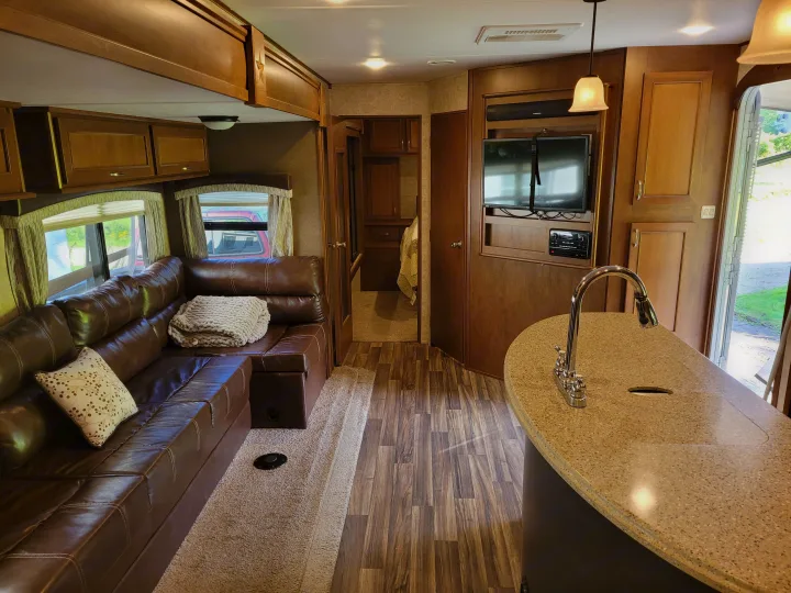 Modern RV rental interior: large leather couch, kitchen island with sink, TV, and wood floors for comfortable living.. Highland Ridge RV Roamer 2016