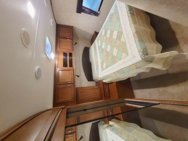 Cozy RV rental bedroom featuring a patterned quilt on the bed, wooden storage, and bright interior lighting.. Highland Ridge RV Roamer 2016