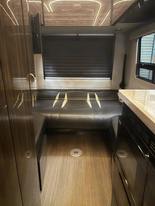 An RV rental interior featuring a convertible seating area, dark window blinds, modern countertop, and wood-look flooring.. Winnebago Era 2017