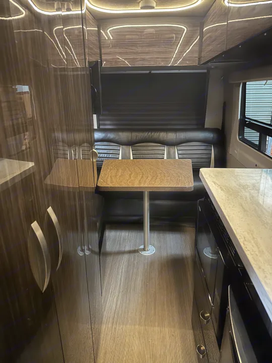 Inside a modern RV rental: a cozy dinette with dark seating & wood-look table, sleek dark cabinets, and integrated overhead lighting.. Winnebago Era 2017
