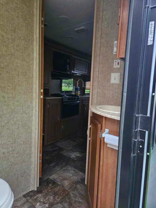 RV rental interior: View of the functional kitchen with stove, microwave, sink, and a compact bathroom vanity.. Coachmen Apex 50th Anniversary 2015