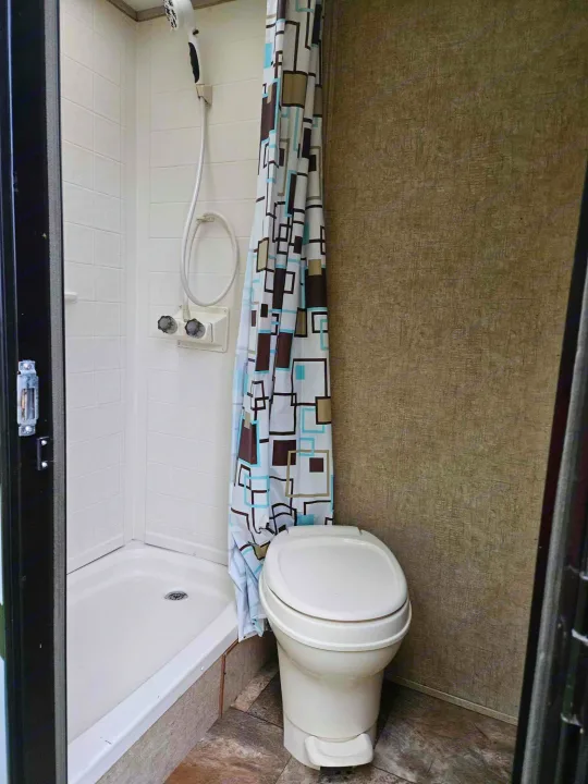 Compact RV rental bathroom featuring a white shower with a patterned curtain and a toilet. Ideal for travel comfort.. Coachmen Apex 50th Anniversary 2015