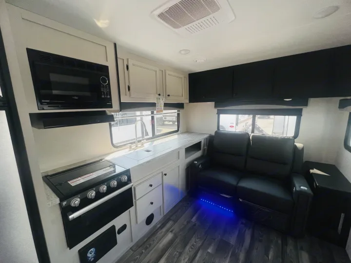 Step into this modern RV rental's bright interior: a well-equipped kitchen with stove, microwave, and plush living recliners with blue lighting.. Highland Ridge RV Range Lite 2022