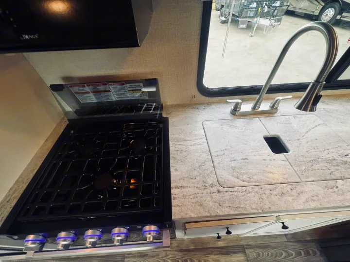 Modern RV kitchen interior with stovetop, sink, and microwave. Perfect for your next rv rental adventure.. Highland Ridge RV Range Lite 2022