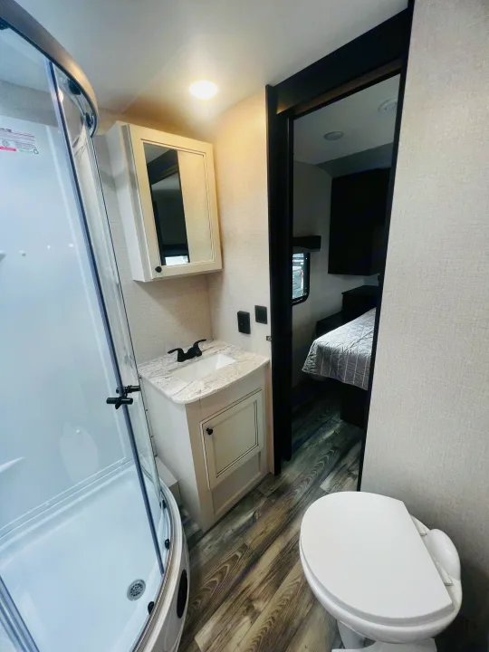 Compact RV rental bathroom with shower, toilet, and sink, offering a peek into the cozy bedroom.. Highland Ridge RV Range Lite 2022