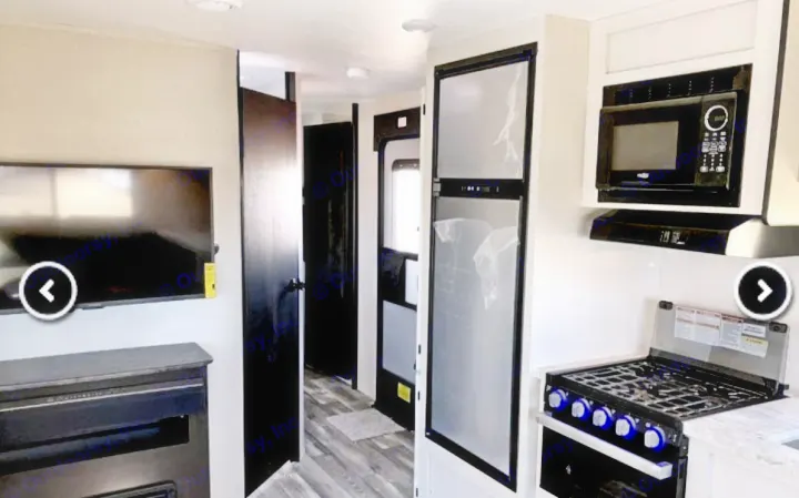 Spacious RV rental interior with a modern kitchen (fridge, stove, microwave) and a living area featuring a TV and fireplace.. Highland Ridge RV Range Lite 2022