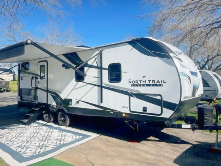 Enjoy an RV rental adventure! Spacious white travel trailer with awning & outdoor rug, perfect for comfortable camping.. Heartland RVs North Trail 2022