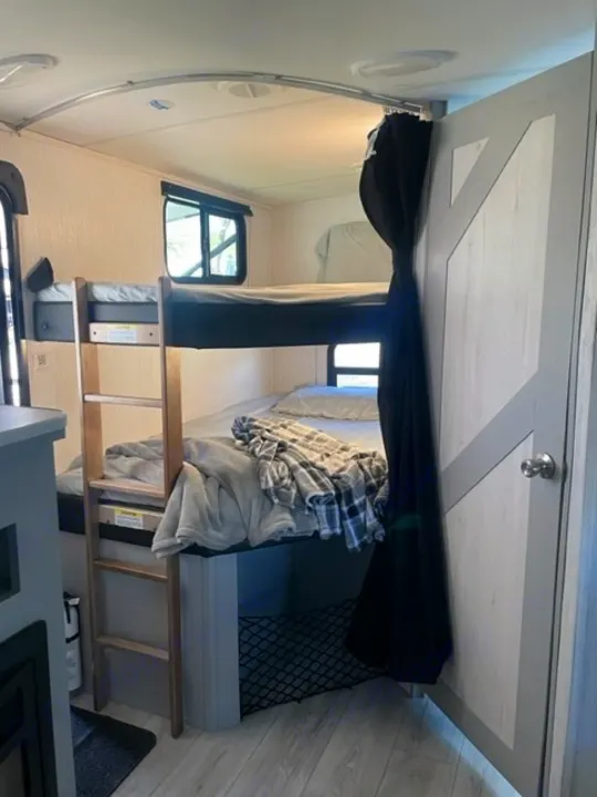 This RV rental shows bunk beds with a ladder, privacy curtain, and storage net, offering a functional sleeping space.. Heartland RVs North Trail 2022