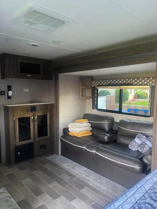 RV rental interior featuring a large leather sofa, patterned window valance, ceiling AC, and plank-style flooring.. Dutchmen Coleman Light 2019