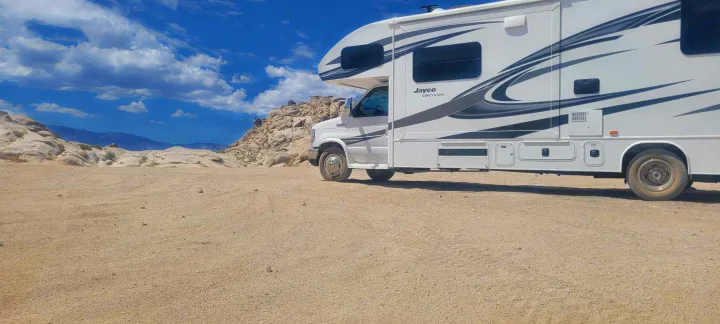 White Jayco Greyhawk RV rental parked on sandy ground with rocks and mountains under a blue sky. Ideal for adventure.. Jayco Greyhawk 2018