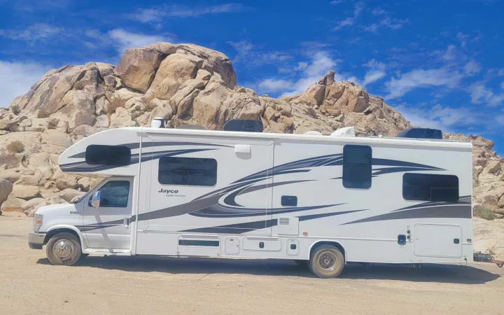 Explore the desert! This rv rental, a white Jayco Greyhawk, is parked among large rock formations under a bright blue sky.. Jayco Greyhawk 2018