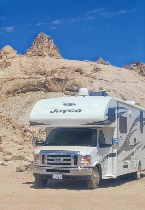 A white Jayco RV rental is parked in a rugged rocky desert landscape under a clear blue sky, ready for adventure.. Jayco Greyhawk 2018