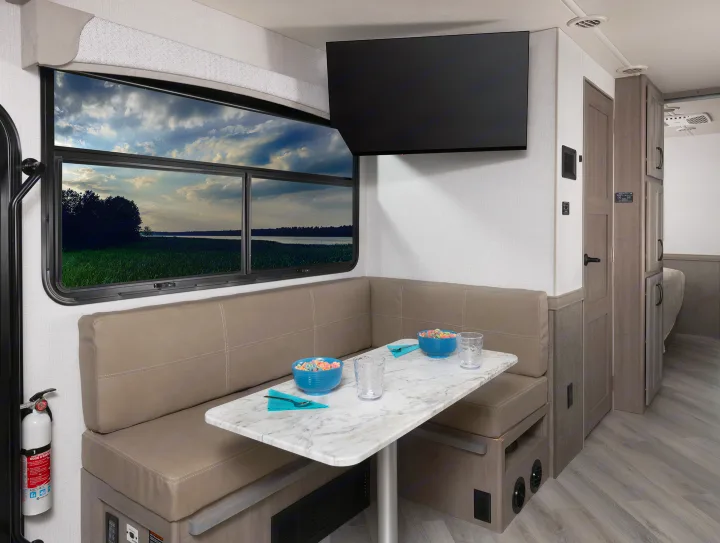Inside an rv rental: a bright dinette area with a scenic window, wall-mounted TV, and cozy bench seating.. Fleetwood Fortis 2024