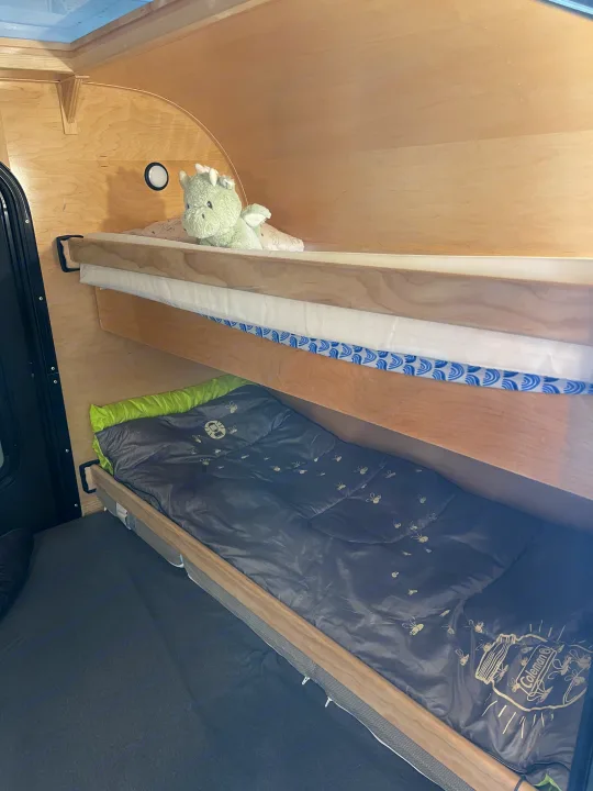 Cozy bunk beds inside an RV rental, with a stuffed dragon on the top bunk and a Coleman sleeping bag below. Ideal for camping.. Other Other 2022