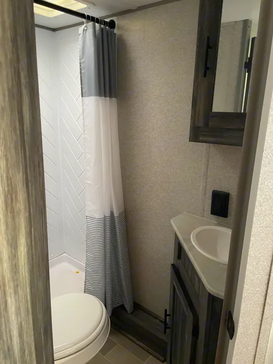 This RV rental bathroom features a compact shower with herringbone walls, a toilet, and a vanity with sink and mirror.. Forest River Salem FSX 2020