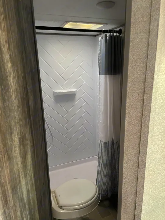 Clean RV rental bathroom. Features a compact toilet, herringbone-tiled shower, and a modern striped curtain.. Forest River Salem FSX 2020