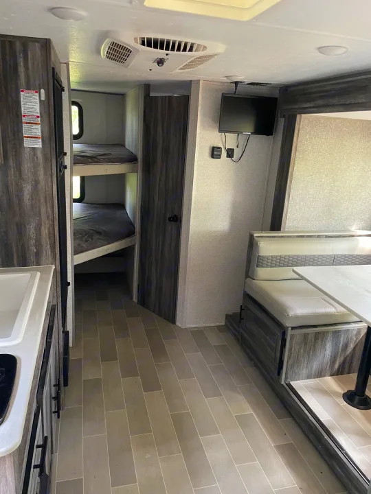 Modern rv rental interior: bunk beds, dinette seating, kitchen counter, wall-mounted TV, and overhead AC unit.. Forest River Salem FSX 2020