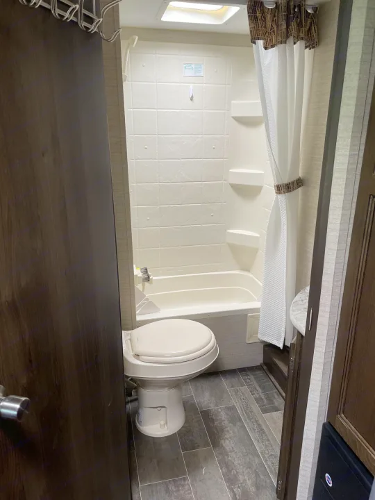 This compact RV rental bathroom features a toilet, shower/tub combo, and wood-look flooring.. Keystone RV Bullet Crossfire 2019