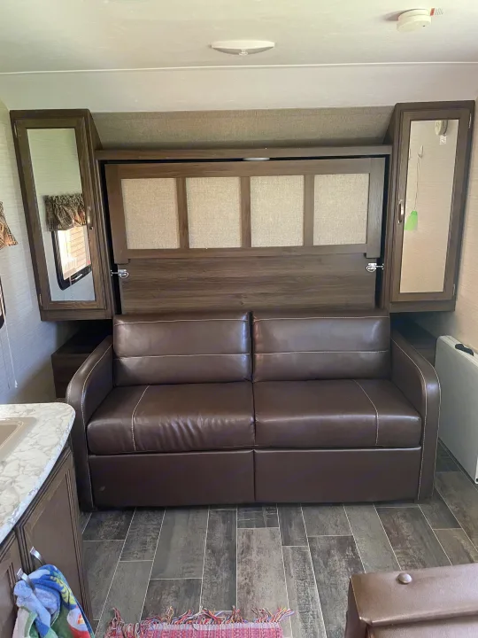 Inside an RV rental: a brown sofa converts to a bed, flanked by wood cabinets. Functional design for travel living.. Keystone RV Bullet Crossfire 2019