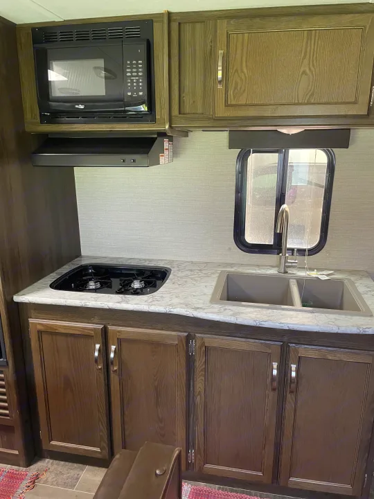 Inside an RV rental: a well-equipped kitchen with microwave, two-burner cooktop, double sink, and ample cabinet space.. Keystone RV Bullet Crossfire 2019