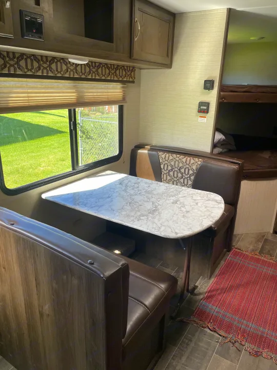 Cozy RV rental interior featuring a dinette with marble-look table, window view, and bunk beds. Ideal camper comfort.. Keystone RV Bullet Crossfire 2019