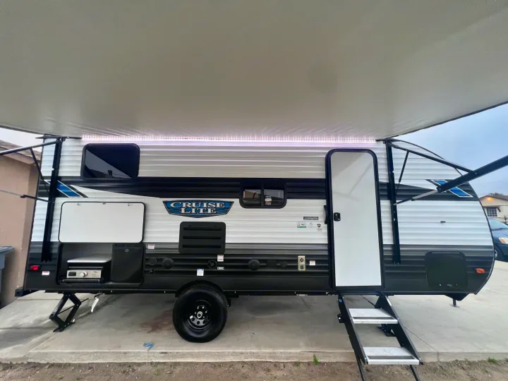 This travel trailer RV rental showcases an extended awning with LED lights, entry steps, and an outdoor kitchen area.. Forest River Salem Cruise Lite 2024