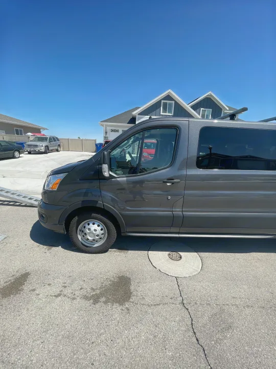 Spacious dark gray van, ideal for RV rental trips, with a roof rack parked on a sunny residential street.. Ford Transit 350 XLT 2020