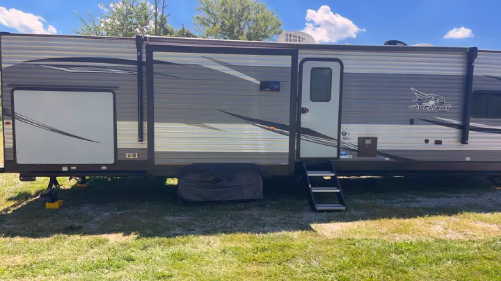 A grey Jay Flight travel trailer, an ideal rv rental, parked on grass and fully setup for a sunny outdoor camping trip.. Jayco Jay Flight 2021